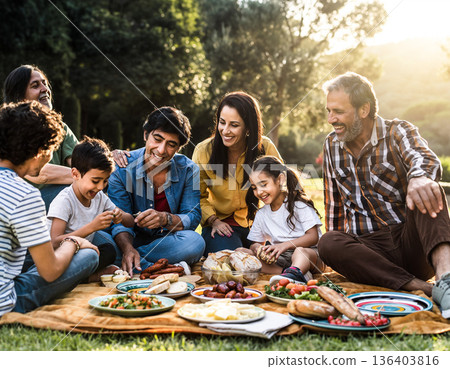 Family gathers outdoors for meal and fun in a sunny park setting with food and laughter 136403816