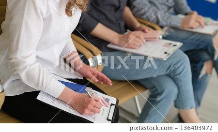 Group of individuals engaged in focused note-taking during a professional meeting in a modern office setting 136403972