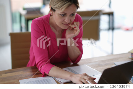 Focused woman working diligently at her desk, lost in thought while engaged with her laptop in a bright, modern workspace Focused woman working diligently at her desk, lost in thought while engaged with her laptop in a bright, modern workspace 136403974