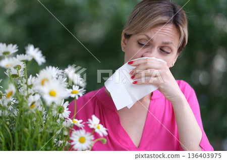 Woman experiencing allergy symptoms while surrounded by blooming daisies in a vibrant garden Woman experiencing allergy symptoms while surrounded by blooming daisies in a vibrant garden 136403975