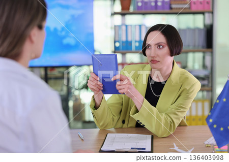 Woman in a vibrant suit discusses important documents with a colleague during a business meeting in a modern office setting 136403998
