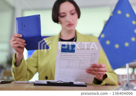 Woman reviews Schengen visa application at a modern office, surrounded by European flags and intent on completing her task 136404006