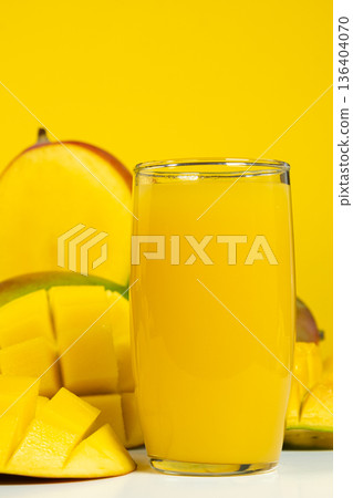Glass of fresh mango juice surrounded by whole and sliced fruits. 136404070