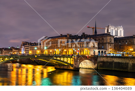 Pont Notre-Dame bridge spans the Seine river leading to the illuminated Hotel-Dieu hospital and Notre-Dame Cathedral under reconstruction at night in Paris, France 136404089