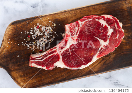 raw rib eye steak, cowboy steak, wooden chopping board, marble table, top view, no people, 136404175