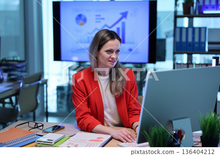 Business professional works on computer in modern office with growth charts displayed in background Business professional works on computer in modern office with growth charts displayed in background 136404212