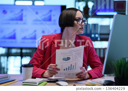Focused analyst reviews data charts and reports in a modern office environment during a busy workday 136404229