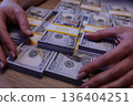 Hands carefully stack bundles of money during a financial transaction in an elegant office setting at dusk 136404251