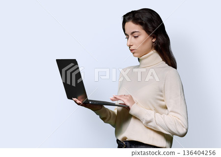 Portrait of serious teenage girl holding laptop on white studio background 136404256