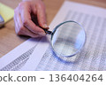 Detailed examination of data with a magnifying glass in a bright workspace 136404264