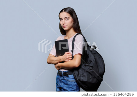Portrait of beautiful female teenage student with backpack, laptop on gray background Portrait of beautiful female teenage student with backpack, laptop on gray background 136404299