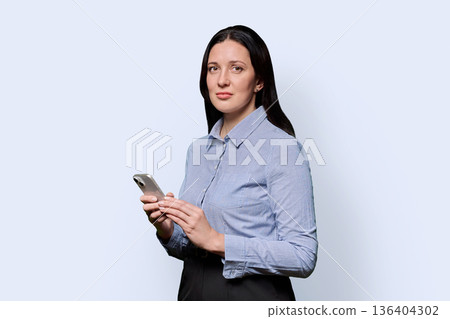 Portrait of successful middle-aged businesswoman with smartphone on light background 136404302