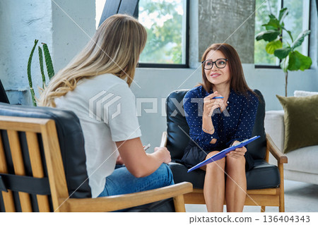 Middle aged professional female psychologist, counselor working with young woman Middle aged professional female psychologist, counselor working with young woman 136404343