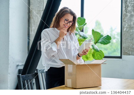 Happy satisfied woman unpacking online purchase, looking at package with cosmetics Happy satisfied woman unpacking online purchase, looking at package with cosmetics 136404437