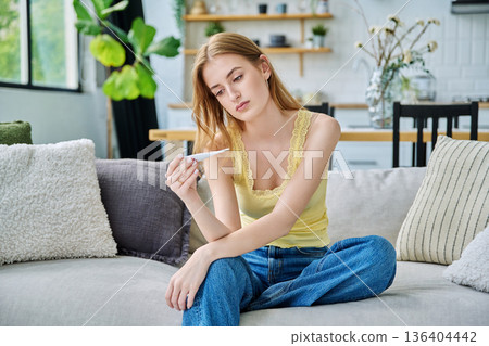 Sad upset teenage girl looking at thermometer sitting at home 136404442