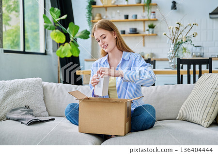 Young happy woman unpacking cardboard box with online order Young happy woman unpacking cardboard box with online order 136404444