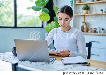 Teenage girl student sitting at the table with laptop, textbooks in home interior 136404451