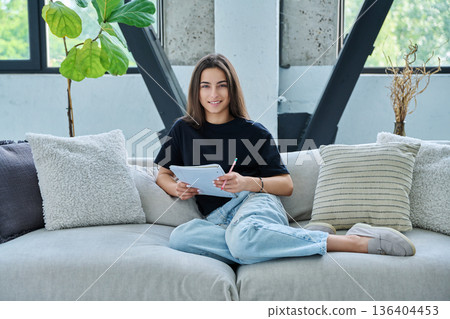 Young student girl study at home, sitting on couch with textbook 136404453