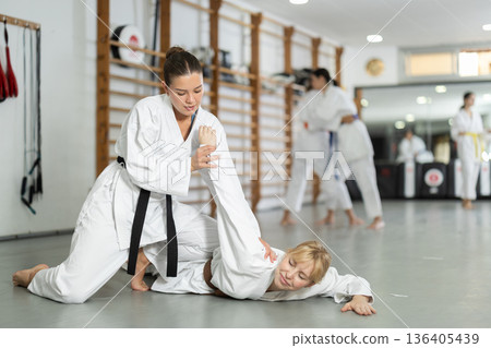 Positive young girl twisting her opponent's arm during judo classes Positive young girl twisting her opponent's arm during judo classes 136405439