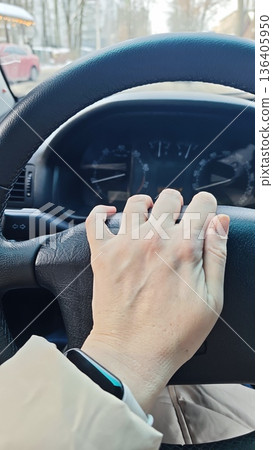 Hand gripping steering wheel inside car with dashboard visible during daytime drive. The image represents the concept of driving, personal transport, control and everyday commuting 136405950