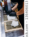 Chef in gloves spreads sushi rice on nori sheets for maki rolls in restaurant kitchen 136406013
