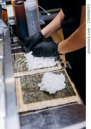 Chef in gloves spreads sushi rice on nori sheets for maki rolls in restaurant kitchen Chef in gloves spreads sushi rice on nori sheets for maki rolls in restaurant kitchen 136406013