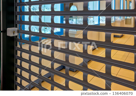 Jewelry store secured with metal roller shutter revealing illuminated luxury display cases inside 136406070