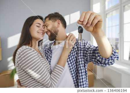 Happy young couple holding a key in their hands standing in a new apartment on moving day. 136406194