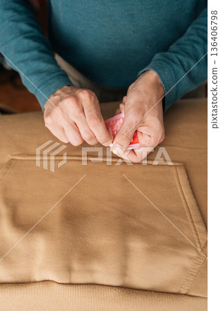 Person opening single-use sachet of cleaning agent, preparing to remove stubborn stain from light brown fabric, focusing on garment care and laundry routine. Concept of household chores. 136406798