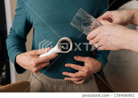 Person holding electric lint remover, operating garment care device on teal sweater to smooth fabric surface and remove pilling, improving textile look. Person holding electric lint remover, operating garment care device on teal sweater to smooth fabric surface and remove pilling, improving textile look. 136406901