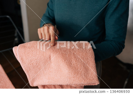 Close-up cropped shot of unrecognizable person inspecting pink towel after washing, scrutinizing visible mark, demonstrating dedication to domestic responsibilities and maintaining household order. 136406930