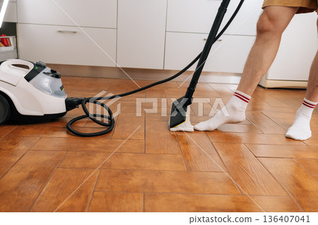 Close-up cropped shot of person using floor cleaner for home hygiene, eliminating germs and dirt from wooden floors, focusing on efficient deep cleaning and fresh living spaces. Close-up cropped shot of person using floor cleaner for home hygiene, eliminating germs and dirt from wooden floors, focusing on efficient deep cleaning and fresh living spaces. 136407041