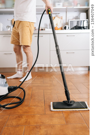 Person using steam cleaner device to sanitize and deep clean kitchen floor, performing domestic chore for efficient home sanitation and hygiene. Concept of maintenance modern home appliance. Person using steam cleaner device to sanitize and deep clean kitchen floor, performing domestic chore for efficient home sanitation and hygiene. Concept of maintenance modern home appliance. 136407049
