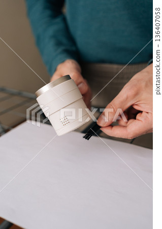 Man holding electric lint remover machine and small brush, preparing for cleaning and maintenance of fabrics, removing fuzz and pills from clothing with the practical device. 136407058