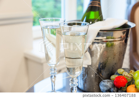 A champagne bottle resting in a frosty ice bucket beside a crystal flutes A champagne bottle resting in a frosty ice bucket beside a crystal flutes 136407188