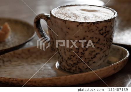A close-up of a speckled ceramic coffee cup resting on a matching plate 136407189