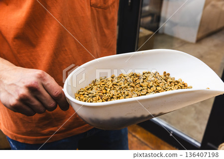 A hand grips a curved white bowl filled with green coffee beans 136407198