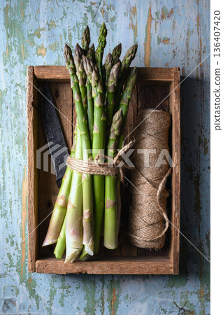 Fresh green asparagus bundle arranged inside wooden crate with twine and knife Fresh green asparagus bundle arranged inside wooden crate with twine and knife 136407420