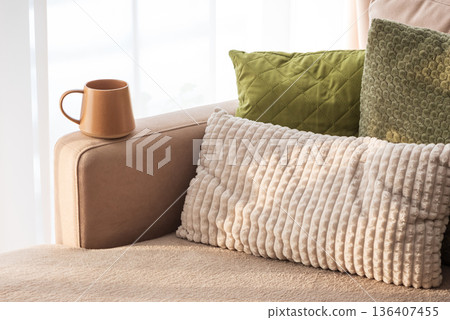 Ceramic Coffee Mug on Sofa Armrest with Textured Pillows. Cozy Home Interior Ceramic Coffee Mug on Sofa Armrest with Textured Pillows. Cozy Home Interior 136407455