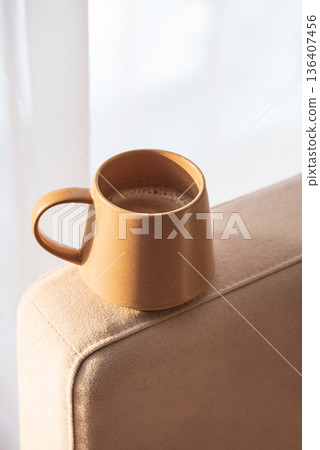 Close Up Ceramic Coffee Mug on Sofa Armrest with Textured Pillows. Cozy Home Interior 136407456