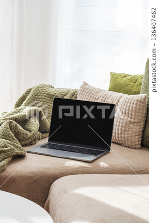 Laptop on Cozy Sofa with Textured Pillows and Blanket. Relaxed Home Workspace Laptop on Cozy Sofa with Textured Pillows and Blanket. Relaxed Home Workspace 136407462