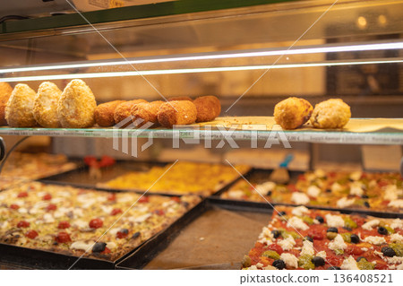 Traditional Italian street food including pizza slices and fried snacks displayed in a bakery showcase in the historic center of Rome. Italy Traditional Italian street food including pizza slices and fried snacks displayed in a bakery showcase in the historic center of Rome. Italy 136408521