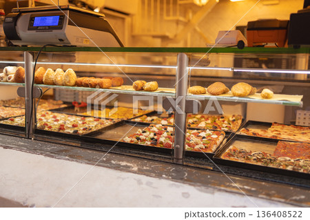 Traditional Italian street food including pizza slices and fried snacks displayed in a bakery showcase in the historic center of Rome. Italy Traditional Italian street food including pizza slices and fried snacks displayed in a bakery showcase in the historic center of Rome. Italy 136408522