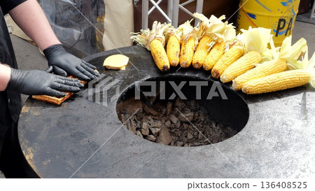 Vendor flipping waffles, Cook flips waffles by corn, Food vendor skillfully flips waffles near corn and barbecue area, Merchant wearing gloves carefully turns waffles beside corn on grill surface Vendor flipping waffles, Cook flips waffles by corn, Food vendor skillfully flips waffles near corn and barbecue area, Merchant wearing gloves carefully turns waffles beside corn on grill surface 136408525