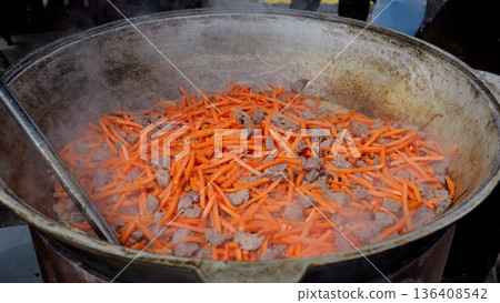 Chef prepares sweet carrots, Gourmet cook garnishes glazed vegetables, Culinary artist finishes glazed carrot topping expertly, Skilled chef decorates with caramelized carrot strips amidst lively 136408542