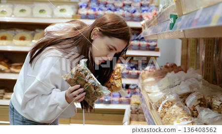 Young woman carefully comparing two bags of bread croutons and reading ingredients before making a purchase decision in the bakery section of a grocery store Young woman carefully comparing two bags of bread croutons and reading ingredients before making a purchase decision in the bakery section of a grocery store 136408562