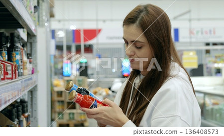 Customer carefully comparing two jars of sauce in a supermarket, reading labels and ingredients 136408573