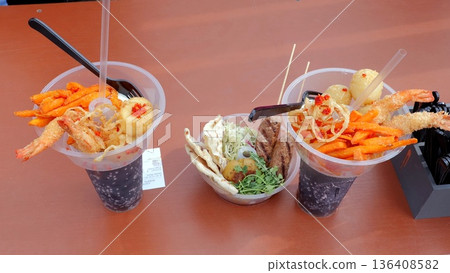 Closeup seafood cups with lemon, crispy tempura shrimp, noodle salad, sliced chili and creamy sauce, camera gear visible suggesting tasting review, warm natural light and casual outdoor festival table Closeup seafood cups with lemon, crispy tempura shrimp, noodle salad, sliced chili and creamy sauce, camera gear visible suggesting tasting review, warm natural light and casual outdoor festival table 136408582