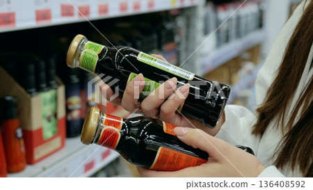 Customer comparing two balsamic vinegar bottles, examining labels and deciding on purchase in grocery store, selective focus Customer comparing two balsamic vinegar bottles, examining labels and deciding on purchase in grocery store, selective focus 136408592