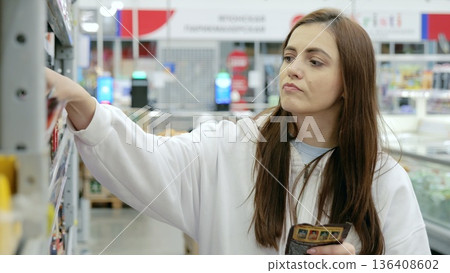 Image of a woman carefully reading labels and selecting healthy products in a supermarket, demonstrating mindful consumer choices in a retail setting Image of a woman carefully reading labels and selecting healthy products in a supermarket, demonstrating mindful consumer choices in a retail setting 136408602